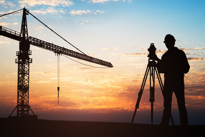 Surveyor-Standing-With-Equipment-At-Construction-Site-921352670_3869x2579